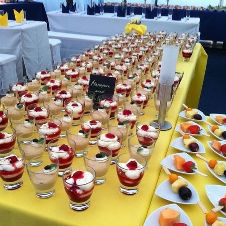 Dessert im Glas mit Beeren und Creme, dekorativ auf Buffet mit gelber Tischdecke angerichtet